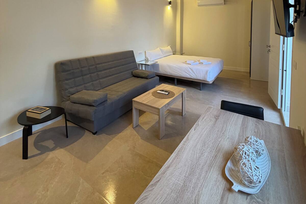 A modern room with a sofa, a bed, a small table, and a TV mounted on the wall.