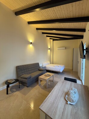 A modern room with a sofa, a bed, a small table, and a TV mounted on the wall.