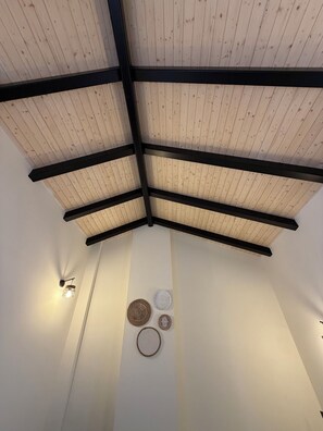 A room with a wooden ceiling, black beams, and wall-mounted light fixtures.