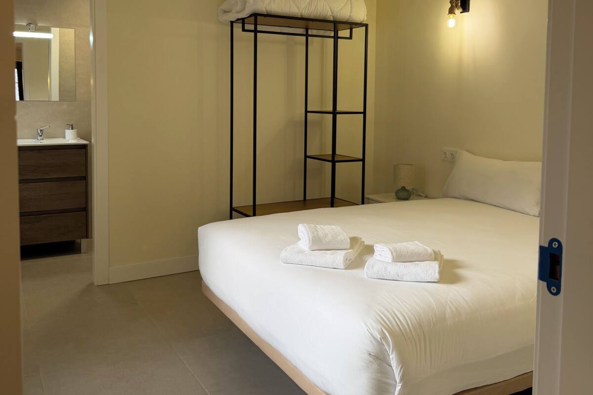 A bedroom with a bunk bed, a bedside table, a lamp, and a bathroom visible through an open door.