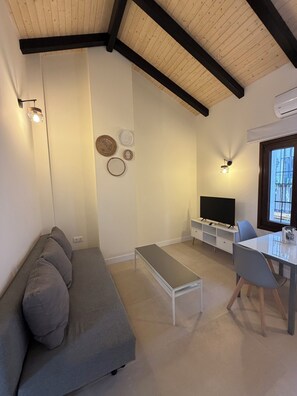 A modern living room with a grey sofa, a small white table, a TV, and wall-mounted lights. - La Corte de Isabel (Cordoba)