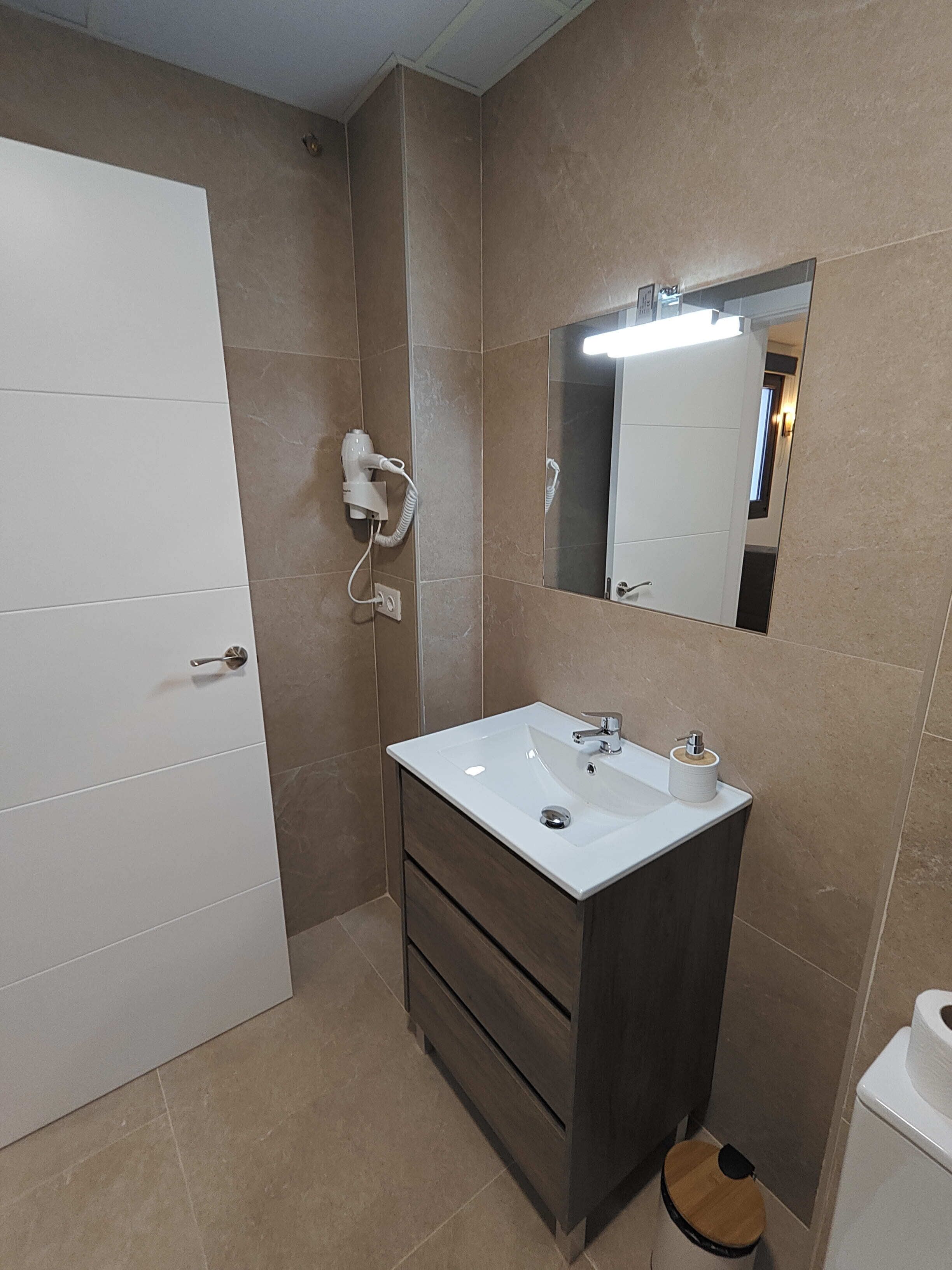 A bathroom with a white sink, dark cabinet, and a mirror above it.