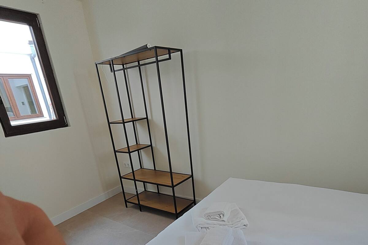 A room with a bed, a metal shelf unit, and a window.