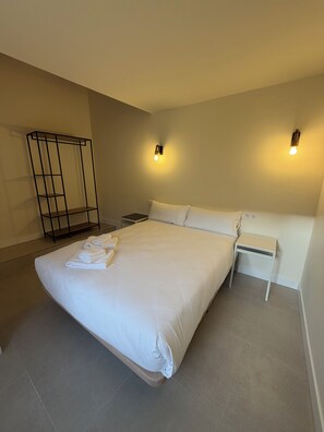 A modern hotel room with a large bed, a bedside table, a nightstand, a wall-mounted light fixture, and a black metal shelf. - La Corte de Isabel (Cordoba)