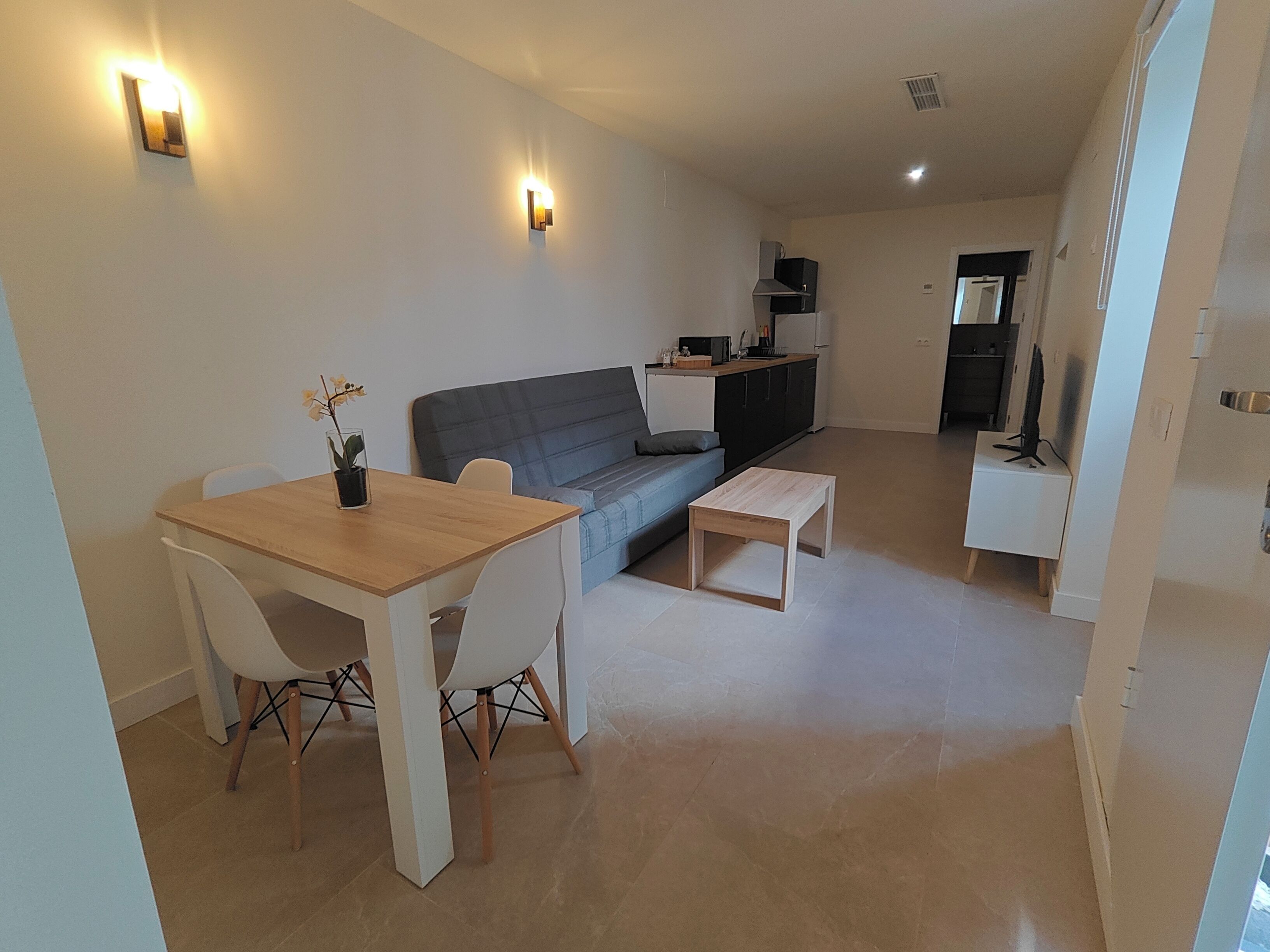 A modern living space with a dining table, sofa, and kitchenette.