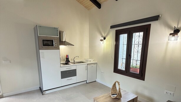 A modern kitchen with built-in appliances, a dining area with a wooden table, and a large window with decorative ironwork. - La Corte de Isabel (Cordoba)