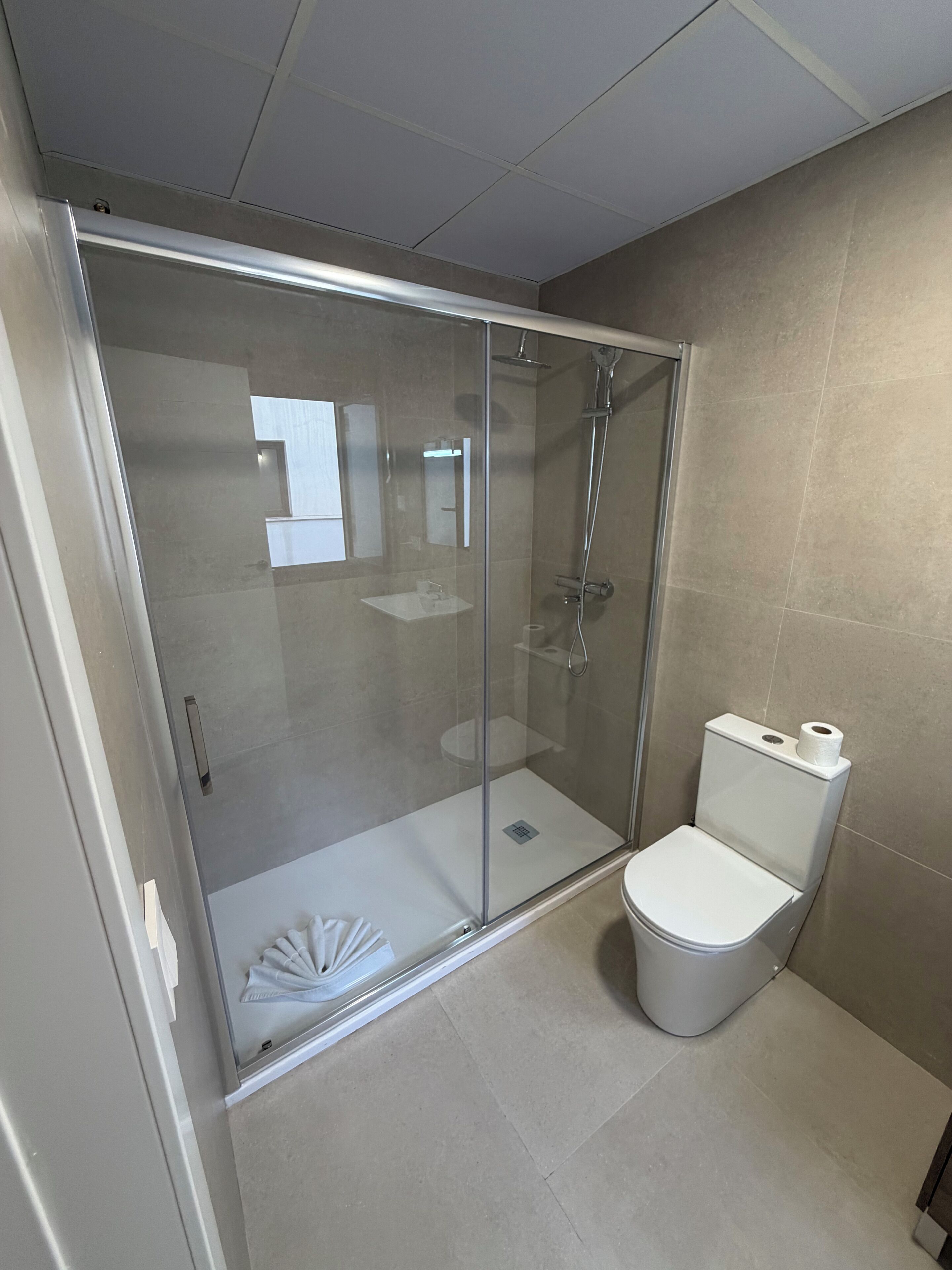 Un baño moderno con cabina de ducha de vidrio, inodoro blanco y lavamanos pequeño.