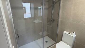 Un baño moderno con cabina de ducha de vidrio, inodoro blanco y lavamanos pequeño.