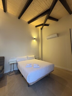 A bedroom with a bed, bedside table, lamp, and an air conditioning unit. - La Corte de Isabel (Cordoba)