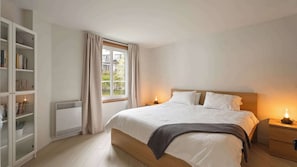 Ein Schlafzimmer mit einem Bett, Nachttischen, einem Bücherregal und einem Fenster mit Vorhängen.
