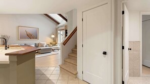 Ein modernes Interieur mit Küchenbereich, einem Wohnzimmer mit Sofa und Couchtisch, einer Treppe und einer weißen Tür.