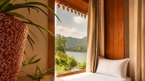 A bedroom with a bed, curtains, a view of a lake, and a plant. - The Lake Heritage Naukuchiyatal (Bhimtal)