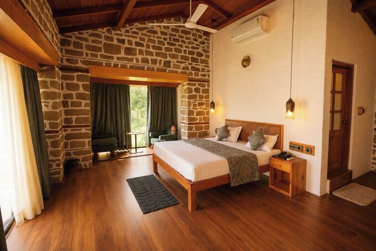 Ein Schlafzimmer mit Steinwand, Holzbalkendecke, einem Bett mit Holzrahmen, einem Nachttisch und einem Fenster mit Vorhängen.