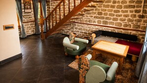 A stone-walled room with a wooden staircase, a sofa, a table, and two chairs. - The Lake Heritage Naukuchiyatal (Bhimtal)