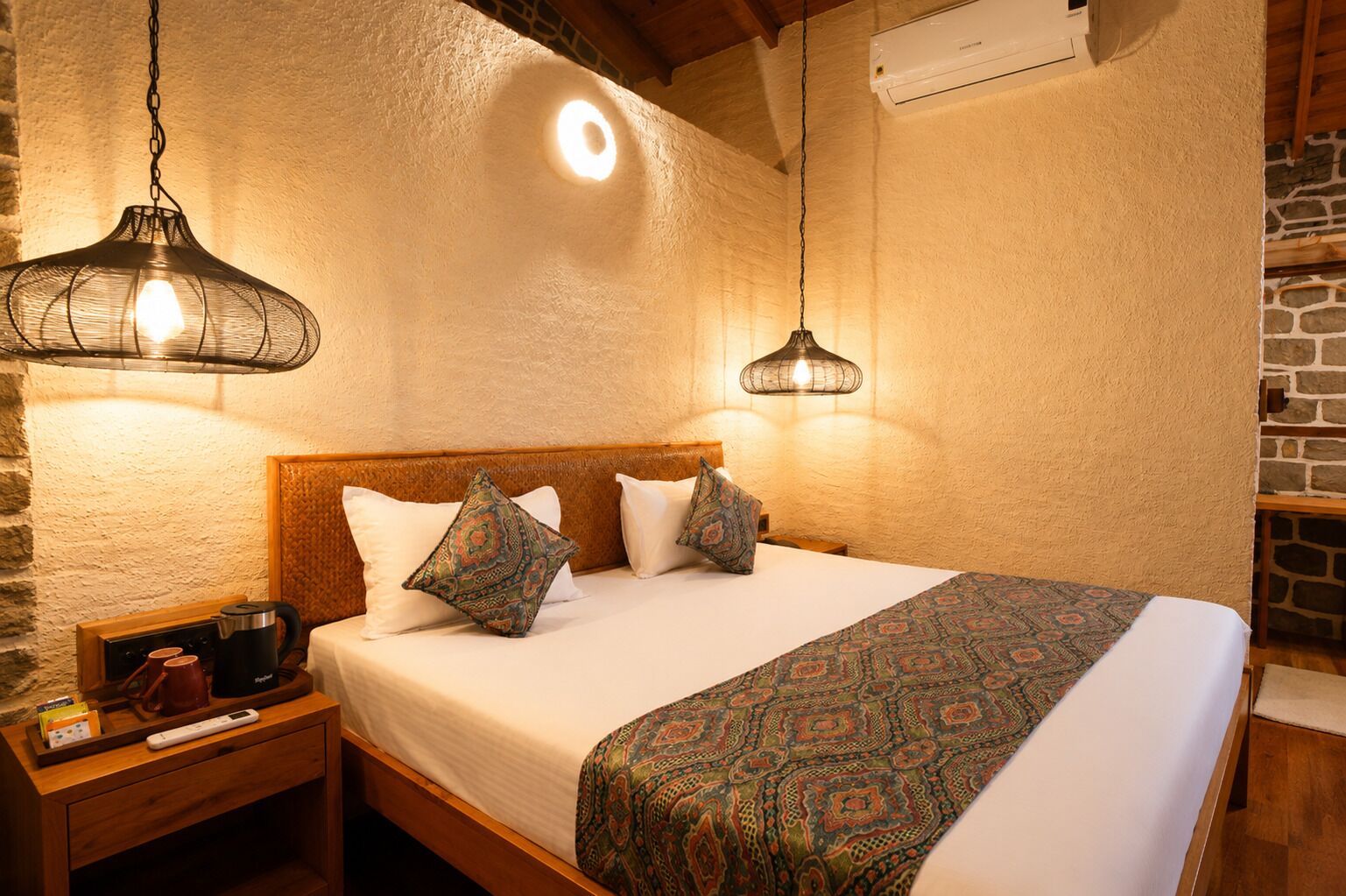 A bedroom with a wooden headboard, patterned bedspread, two decorative pillows, a bedside table with a kettle and cups, and two hanging lamps.