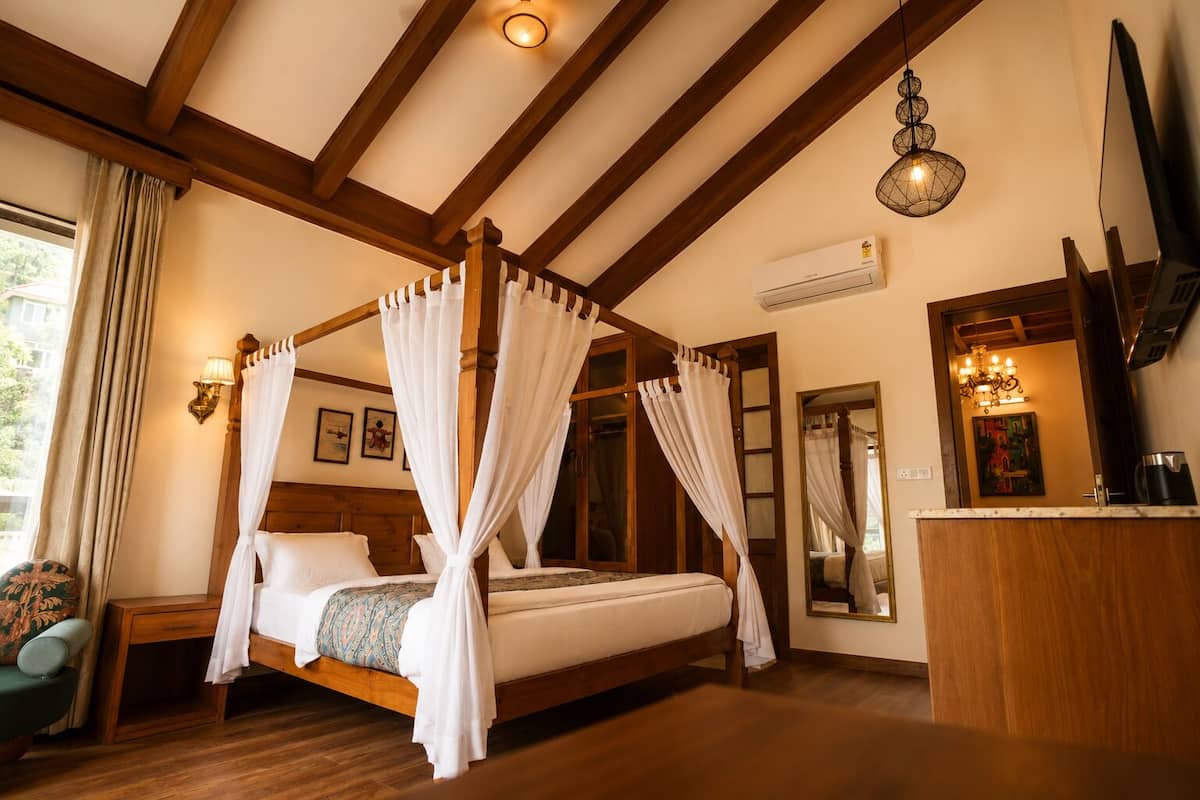 Ein Bett mit Baldachin, weiße Vorhänge, Holzbalken, eine Wandklimaanlage und eine Kristallleuchter.
