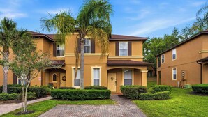 A two-story building with a brick pathway leading to the entrance, surrounded by well-maintained greenery and palm trees. - Casa Palermo At Regal Palms (Davenport)