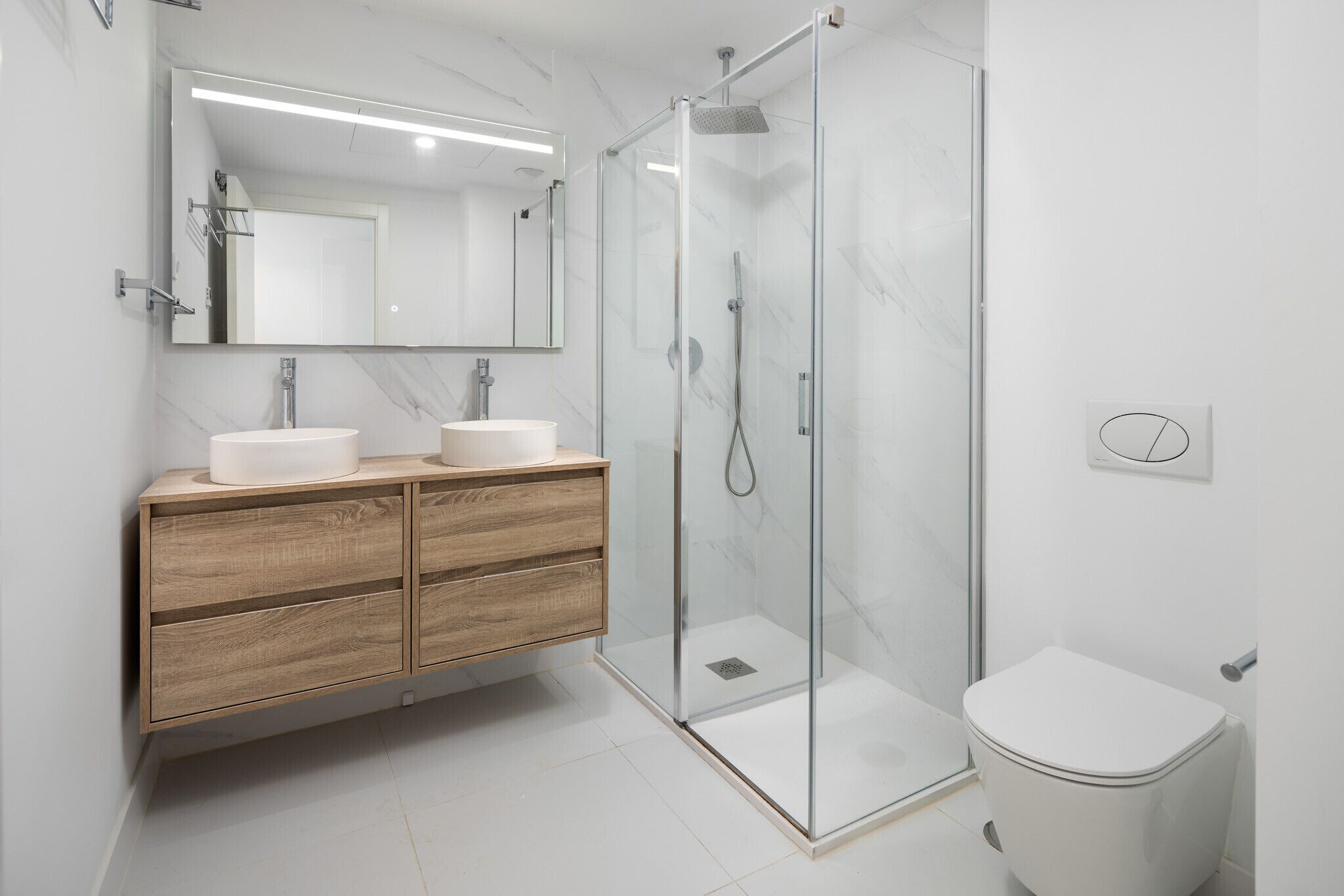 A modern bathroom with a glass-enclosed shower, two sinks, a mirror, and a toilet.