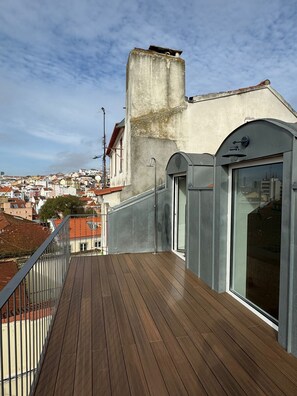 A rooftop terrace with a wooden deck, a concrete wall, and a view of a cityscape. - Santos Design Townhouse by Cadenzalux (Lisbon)