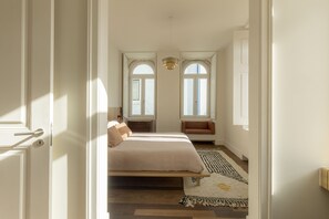 A bedroom with a bed, a bench, a rug, and two windows. - Santos Design Townhouse by Cadenzalux (Lisbon)