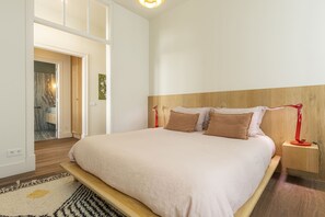A bedroom with a large bed, wooden headboard, bedside tables, and a view of an adjacent bathroom. - Santos Design Townhouse by Cadenzalux (Lisbon)