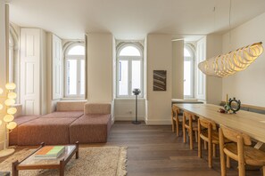 Ein modernes Wohnzimmer mit einer Couch, einem Esstisch mit Stühlen, einer Stehlampe und einem großen Fenster.