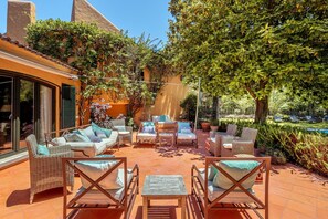Un patio al aire libre con mobiliario de mimbre, una piscina y abundante follaje.