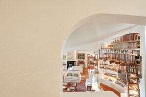 Un salón amplio con chimenea, mobiliario blanco y una gran estantería llena de libros y objetos decorativos.
