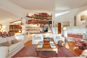 Un salón espacioso con una amplia estantería, sofás blancos y una mesa de centro.