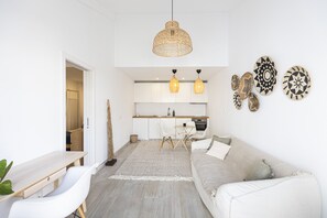 Eine moderne Küche mit weißen Schränken, ein Essbereich mit Tisch und Stühlen sowie ein Wohnbereich mit einer Couch und dekorativen Tellern an der Wand.