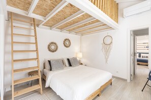 Ein Schlafzimmer mit einer Holzleiter, einem Bett mit weißer Bettwäsche, zwei Wanddekorationen und einem Traumfänger.