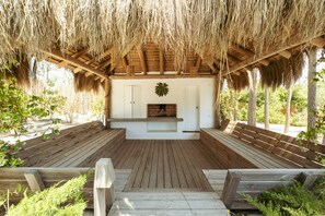 Una terraza exterior de madera con techo de paja, chimenea y bancos.