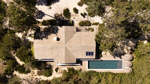 Oversigtsbillede af et moderne hus med symmetrisk design, swimmingpool og skovområde omkring.
