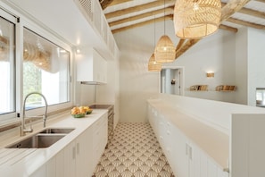 Una cocina moderna con armarios blancos, suelo de estampado geométrico y vigas de madera a la vista.