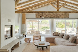 Amplia sala de estar con techo alto, ventanas grandes, chimenea y una disposición de asientos cómoda.