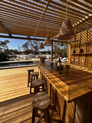 Una terraza de madera con una zona de bar, asientos al aire libre y una piscina.