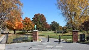 Una entrada al parc amb un camí de maons, una reixa de metall i un cartell que diu "KISSMAN PARK".