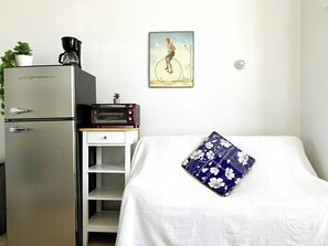 A compact room with a bed, a small kitchenette with a refrigerator, a toaster, and a coffee maker.