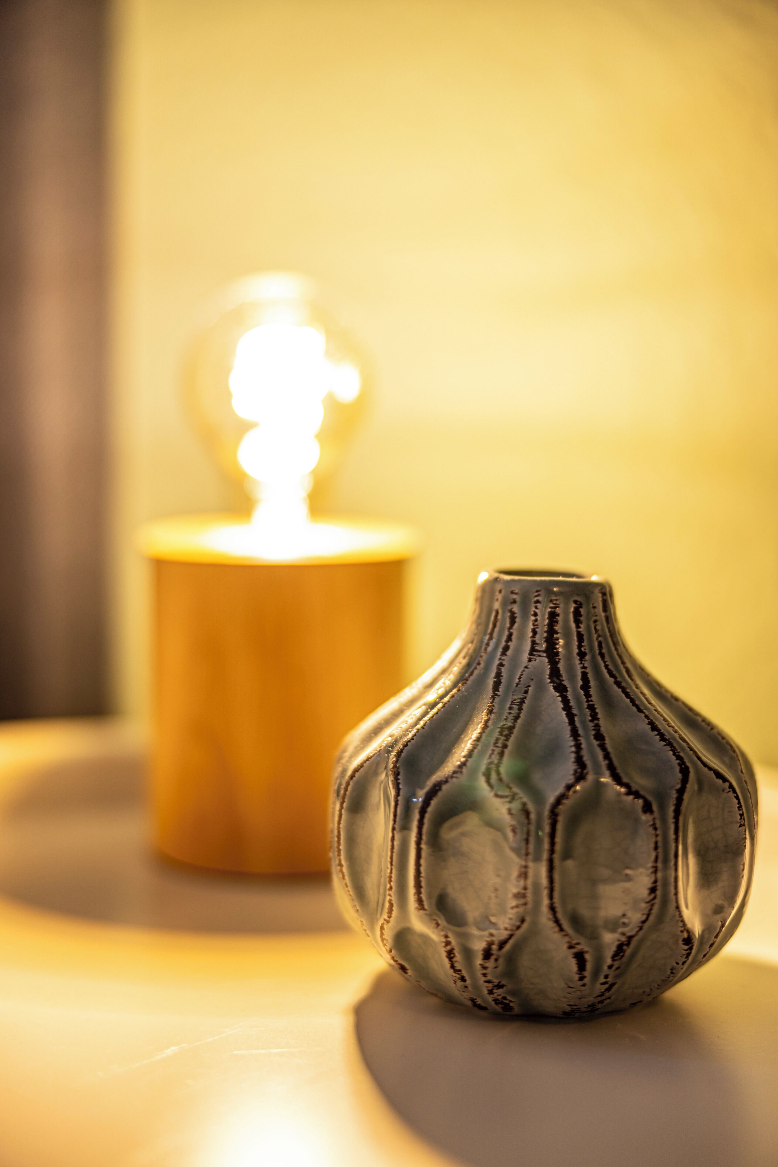 A close-up of a ceramic vase with a textured pattern, placed on a surface with a candle in the background.