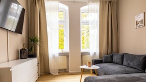A modern bedroom with a sofa, a TV mounted on the wall, a small table, and a window with curtains. - City Apartment-River Old Town-central-WLAN- river view (Erfurt)
