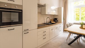 A modern kitchen with white cabinetry, a built-in oven, a sink, and a dining area with a table and chairs. - City Apartment-River Old Town-central-WLAN- river view (Erfurt)