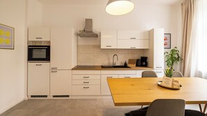 A modern kitchen with white cabinetry, a wooden dining table, a hanging light fixture, and a potted plant. - City Apartment-River Old Town-central-WLAN- river view (Erfurt)