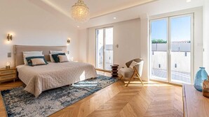 Ein Schlafzimmer mit einem großen Bett, einem Sessel, einem Teppich und Blick durch das Fenster.