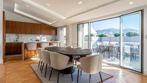 Eine moderne Küche mit Marmorarbeitsplatte, ein Essbereich mit rundem Tisch und Stühlen sowie eine große Schiebeglastür, die auf eine Außenpatio führt.