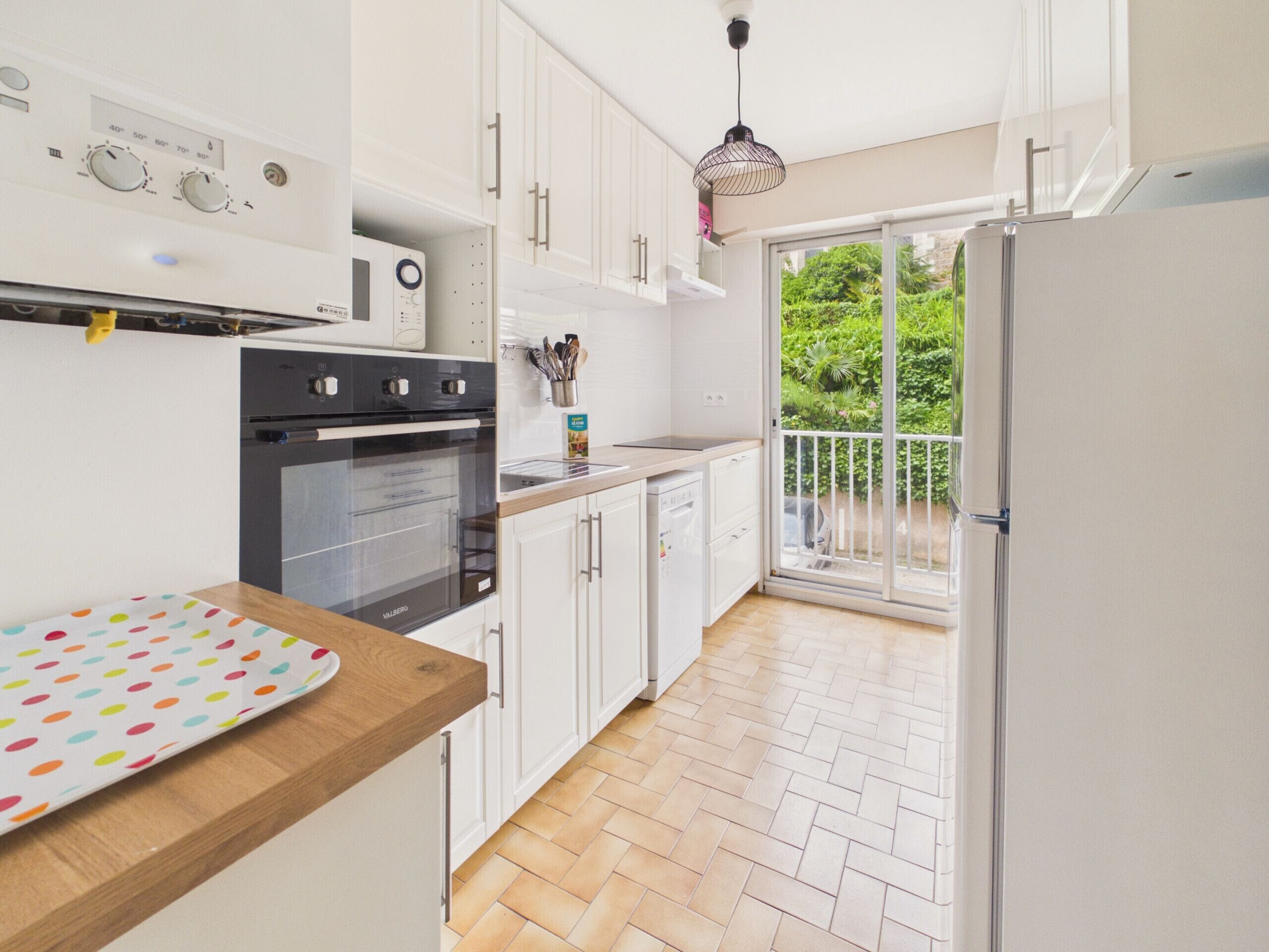 A modern kitchen with white cabinets, a herringbone floor, and a view of greenery through the sliding glass door.