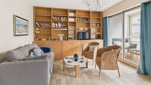 Ein modernes Wohnzimmer mit einer Couch, Sesseln, einem Couchtisch, einem Bücherregal und einem Fernseher.