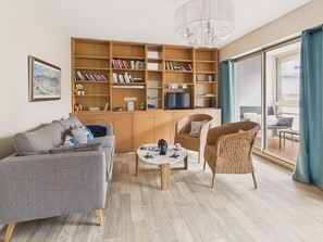 Ein modernes Wohnzimmer mit einer Couch, Sesseln, einem Couchtisch, einem Bücherregal und einem Fernseher.