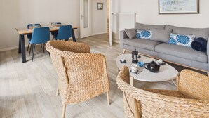 Ein modernes Wohnzimmer mit grauem Sofa, Korbstühlen, einem Esstisch mit Stühlen, einem Couchtisch mit Teekanne und einer Heizung.
