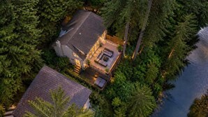 A house surrounded by dense forest, with a visible deck and outdoor seating area. - Capilano Forest Retreat | 3BD/2BA Suite (North Vancouver)