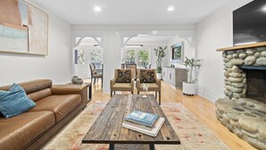 A modern living room with a leather sofa, a coffee table, and a stone fireplace. - Capilano Forest Retreat | 3BD/2BA Suite (North Vancouver)